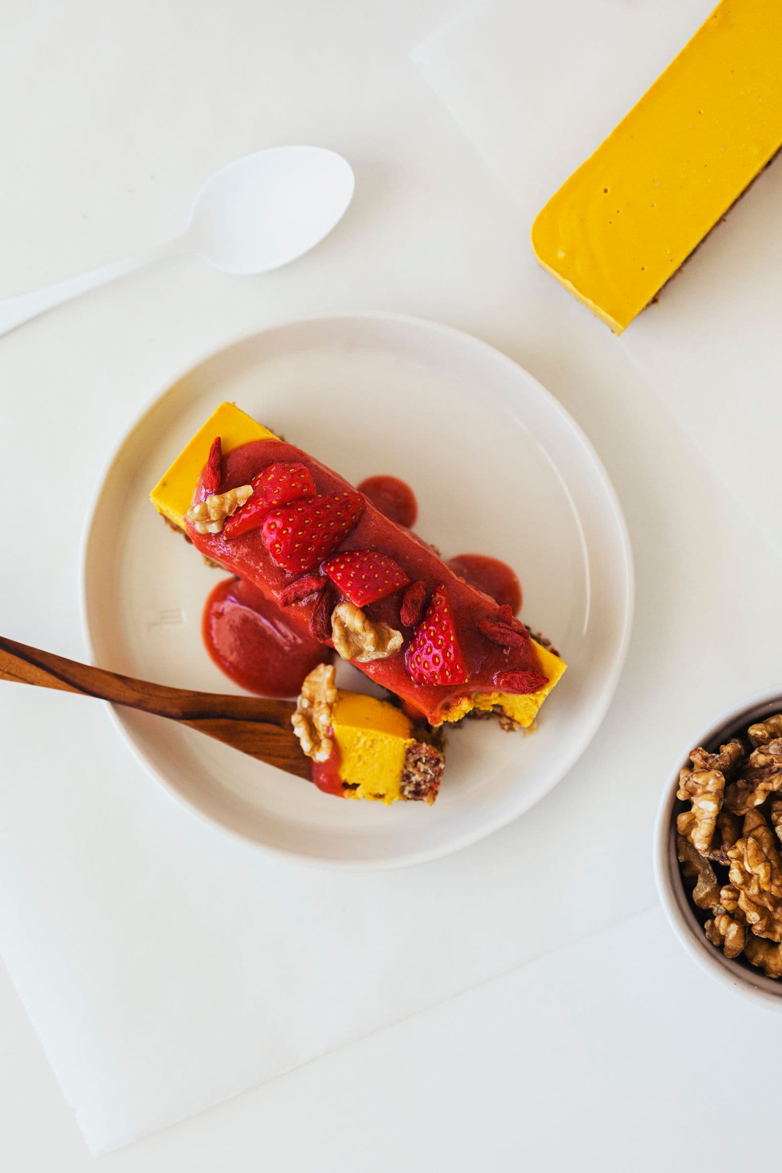 Beautifully decorated raw vegan cheesecake on a small, white dish with a wooden fork.