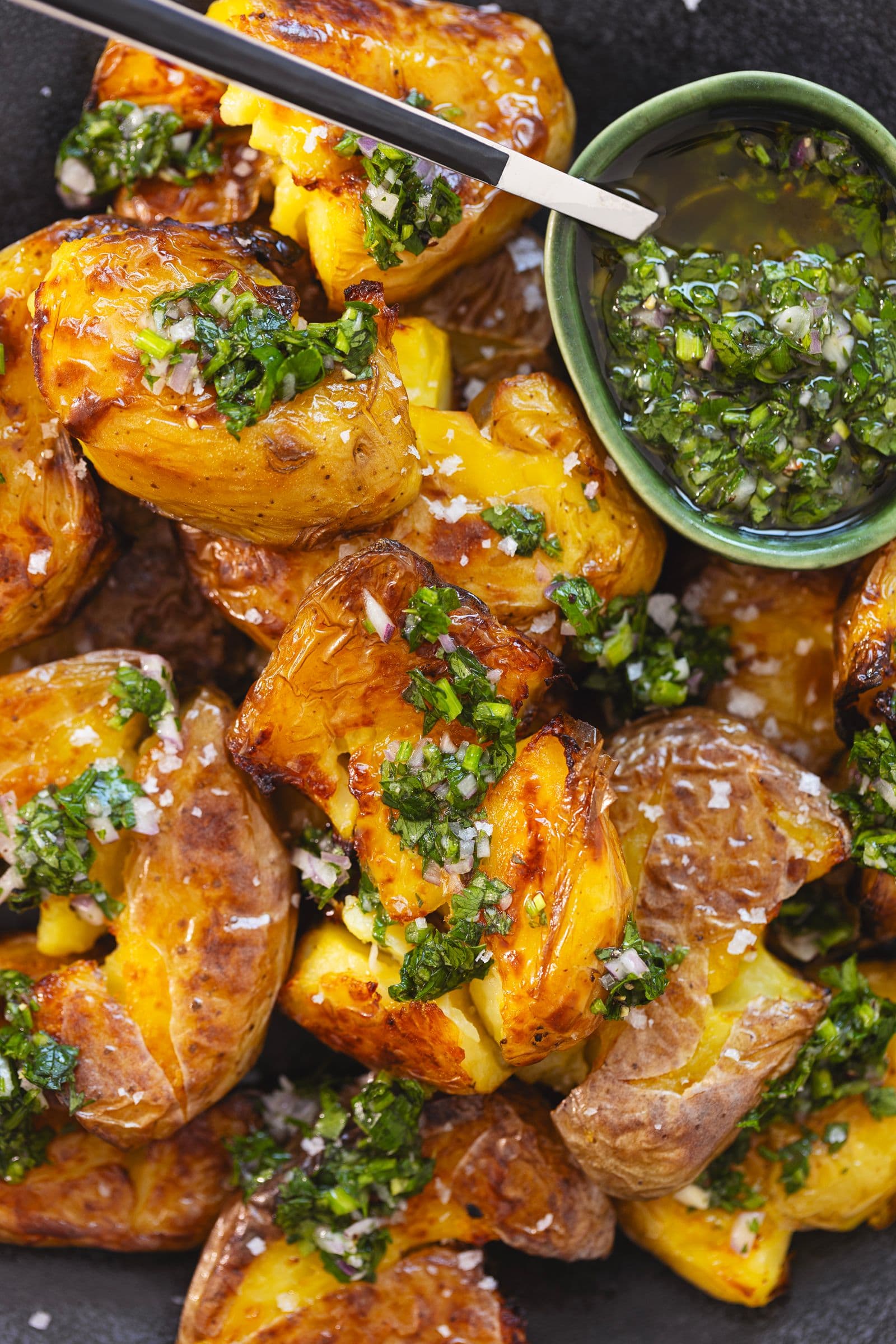 Close-up of golden roasted potatoes with green herb sauce and olive oil
