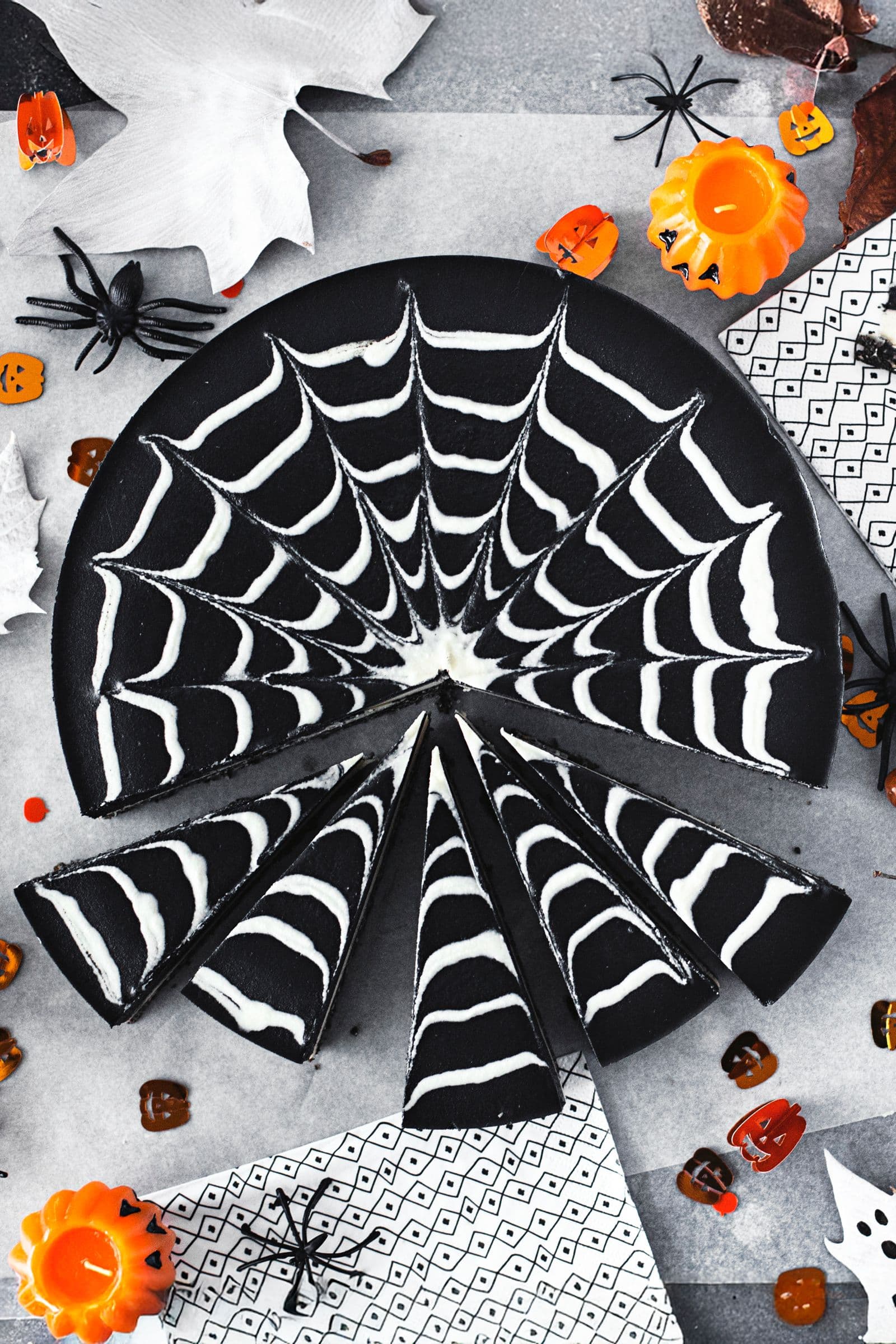 A double chocolate Halloween cheesecake with a spiderweb pattern surrounded by pumpkins, spiders and festive decorations.