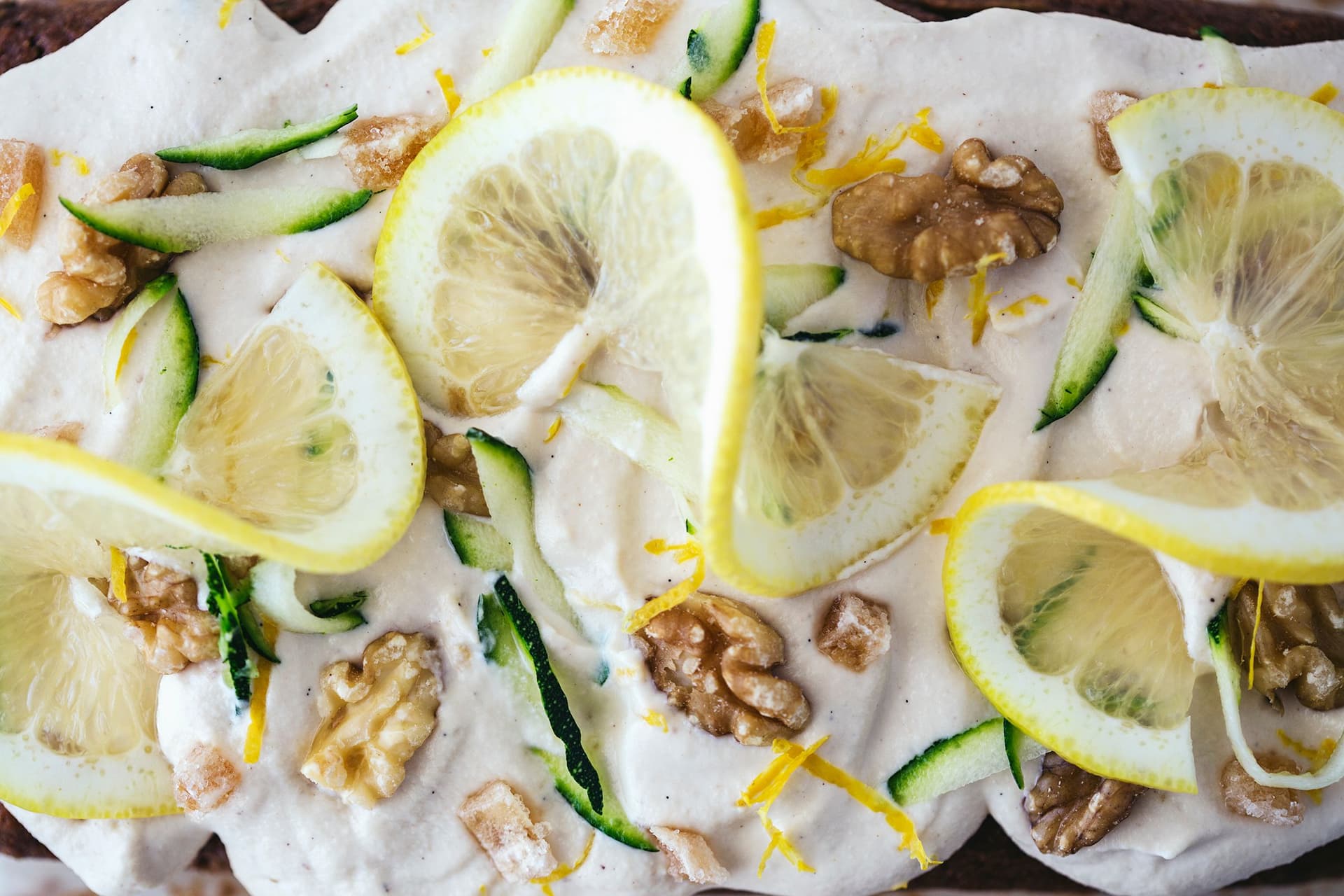 The cake topped with frosting, lemon slices, zucchini ribbons, candied ginger and chopped walnuts.