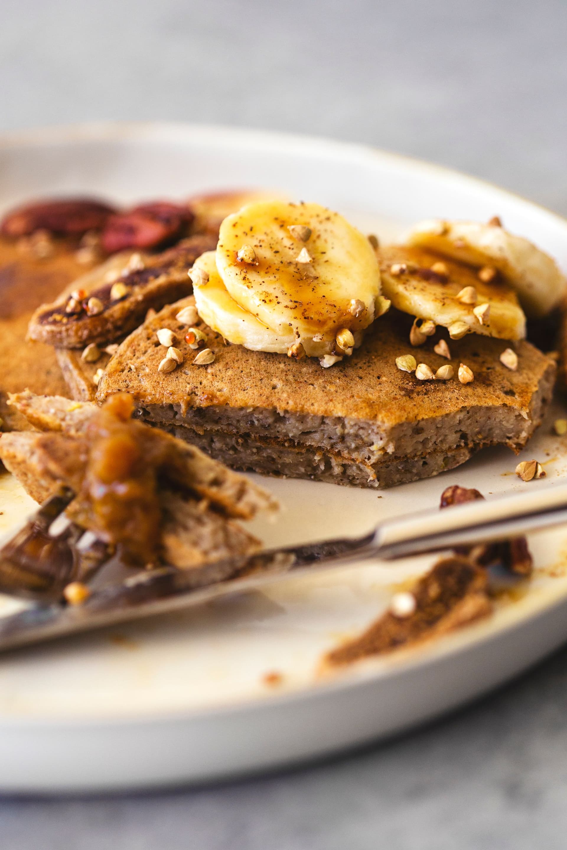 Pancake slice on fork showing fluffy interior with banana topping and drizzle.