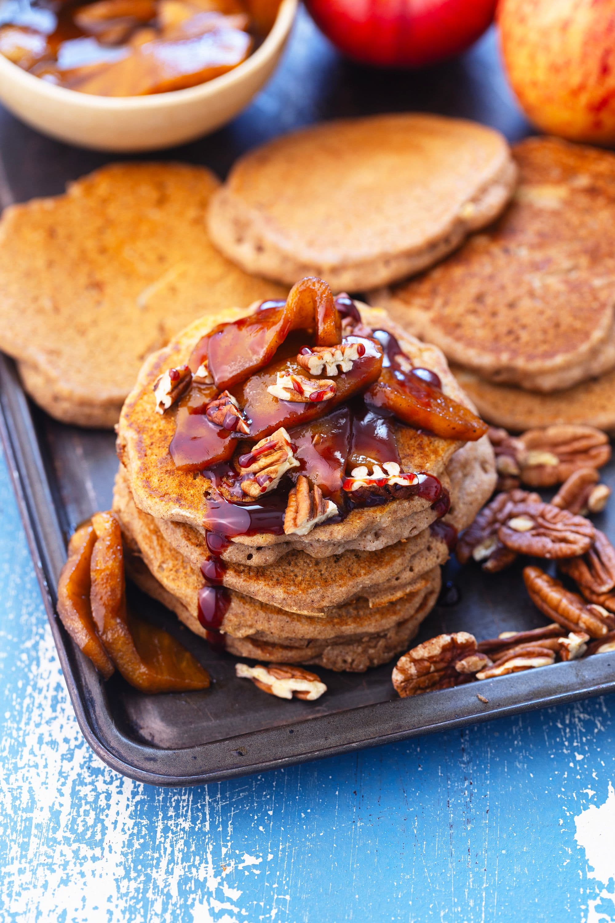 Pilha de panquecas de trigo sarraceno com maçã, cobertas com maçã caramelizada, pecãs e xarope.