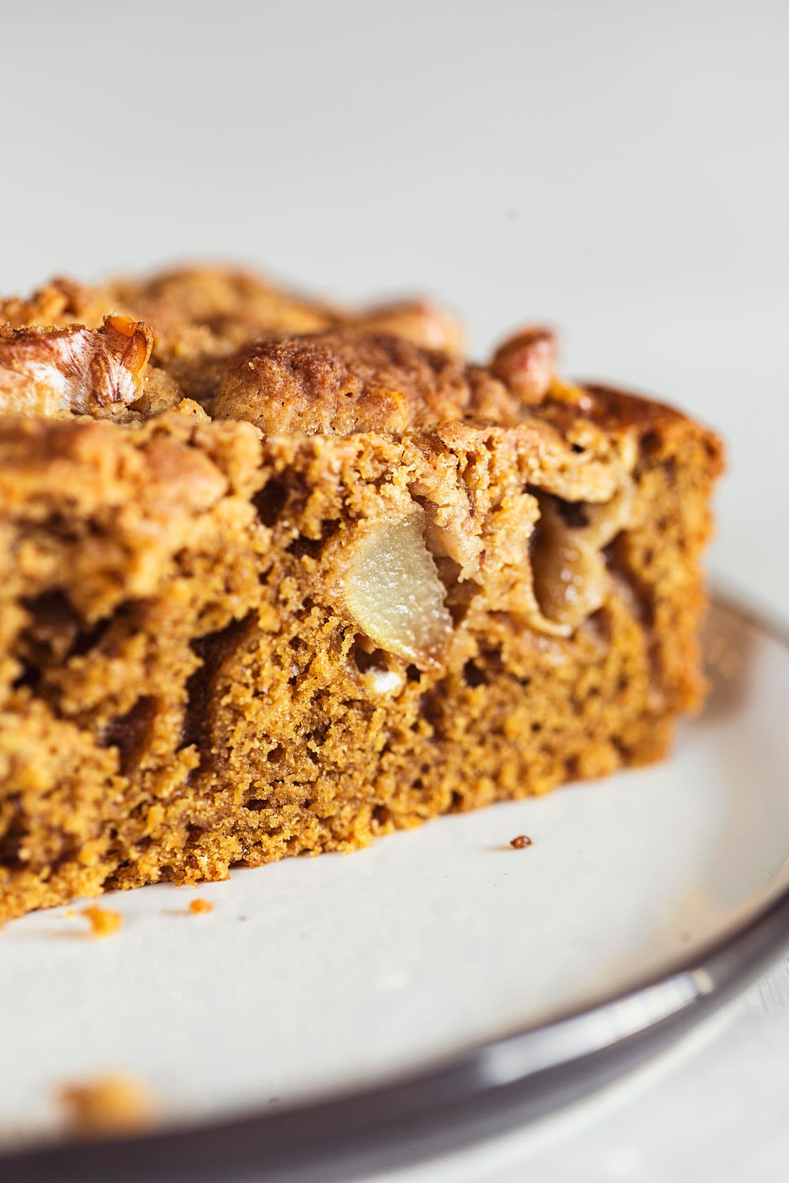 Close-up of a moist coffee and pear cake slice with walnut topping, showing fluffy texture.