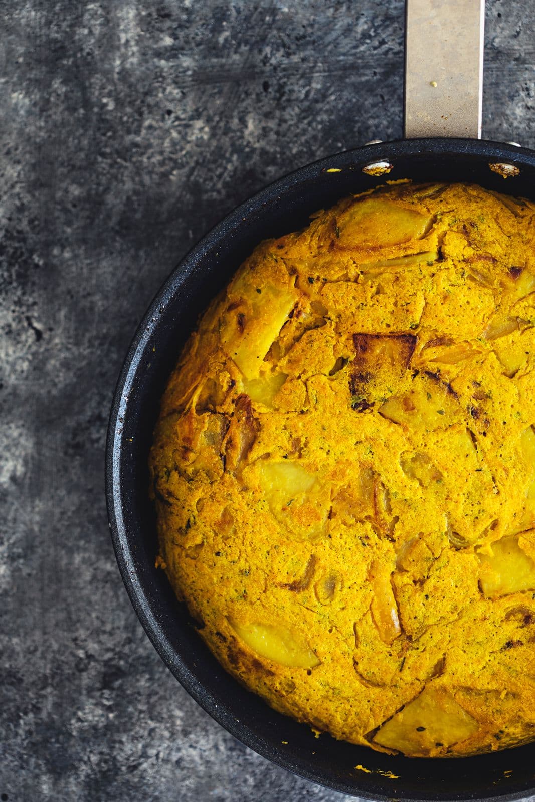 Tortilha vegan cozinhada numa frigideira preta, dourada por cima e pronta a cortar.