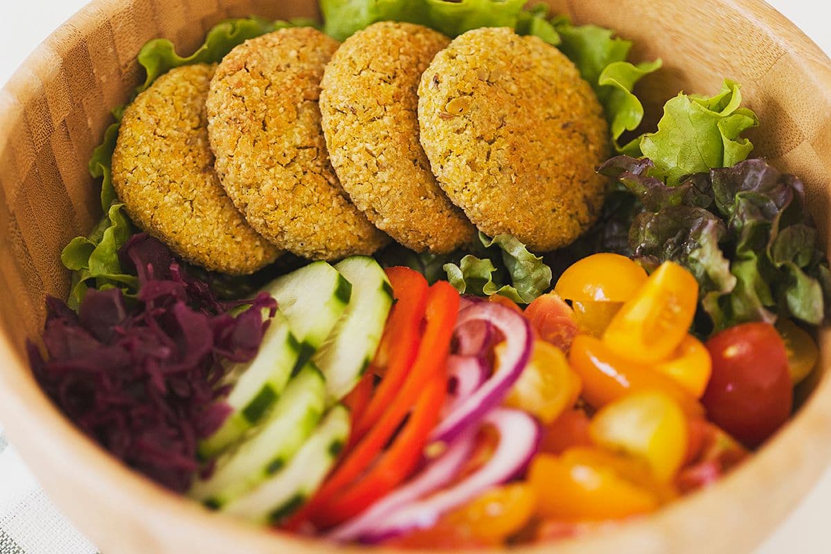 Taça de salada fresca com quatro falafels no topo.