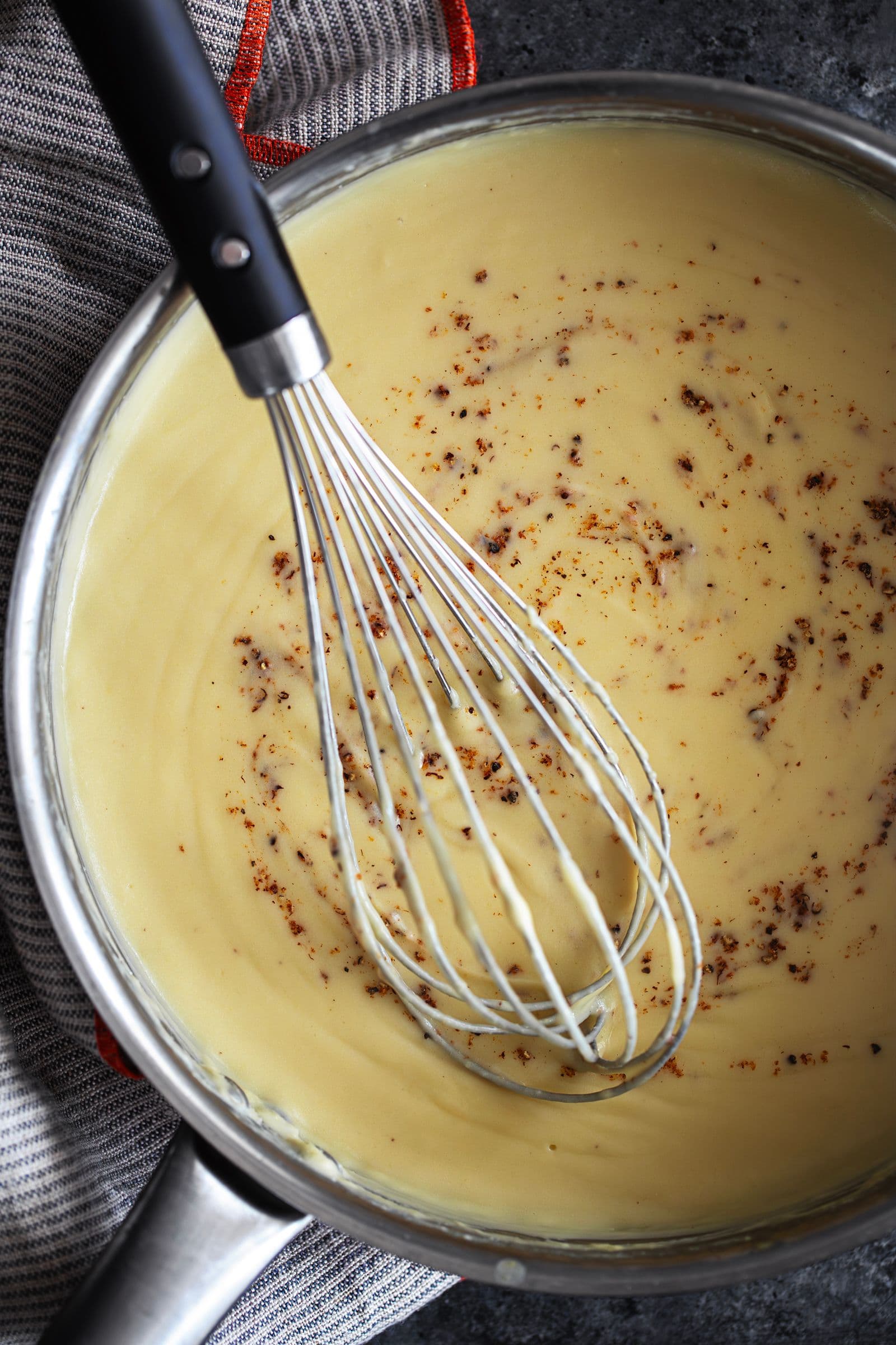 Gluten-free vegan béchamel in a saucepan, stirred with a whisk and sprinkled with nutmeg