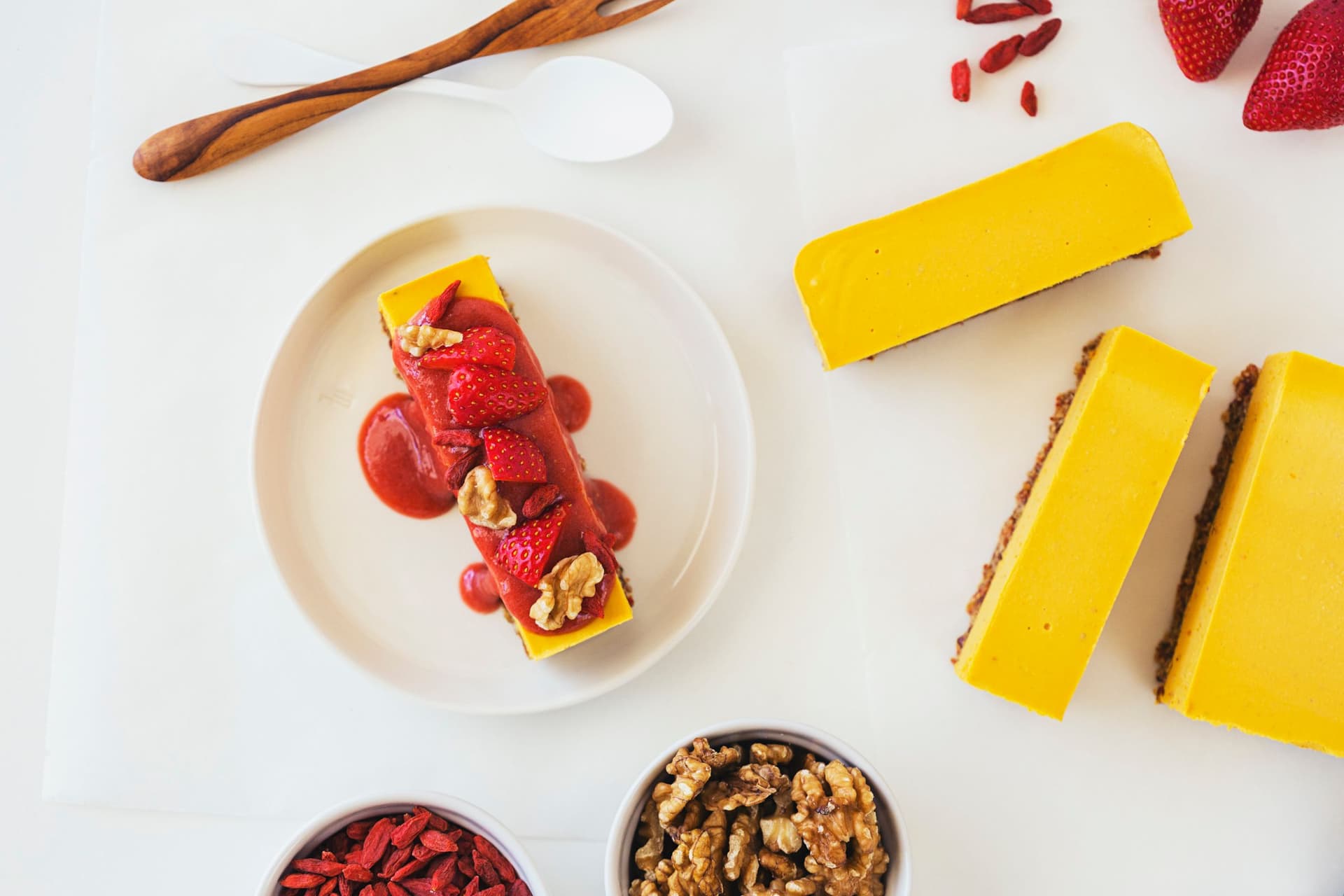 Slice of orange, goji, and strawberry raw vegan cheesecake topped with fresh strawberries, walnuts and sauce.