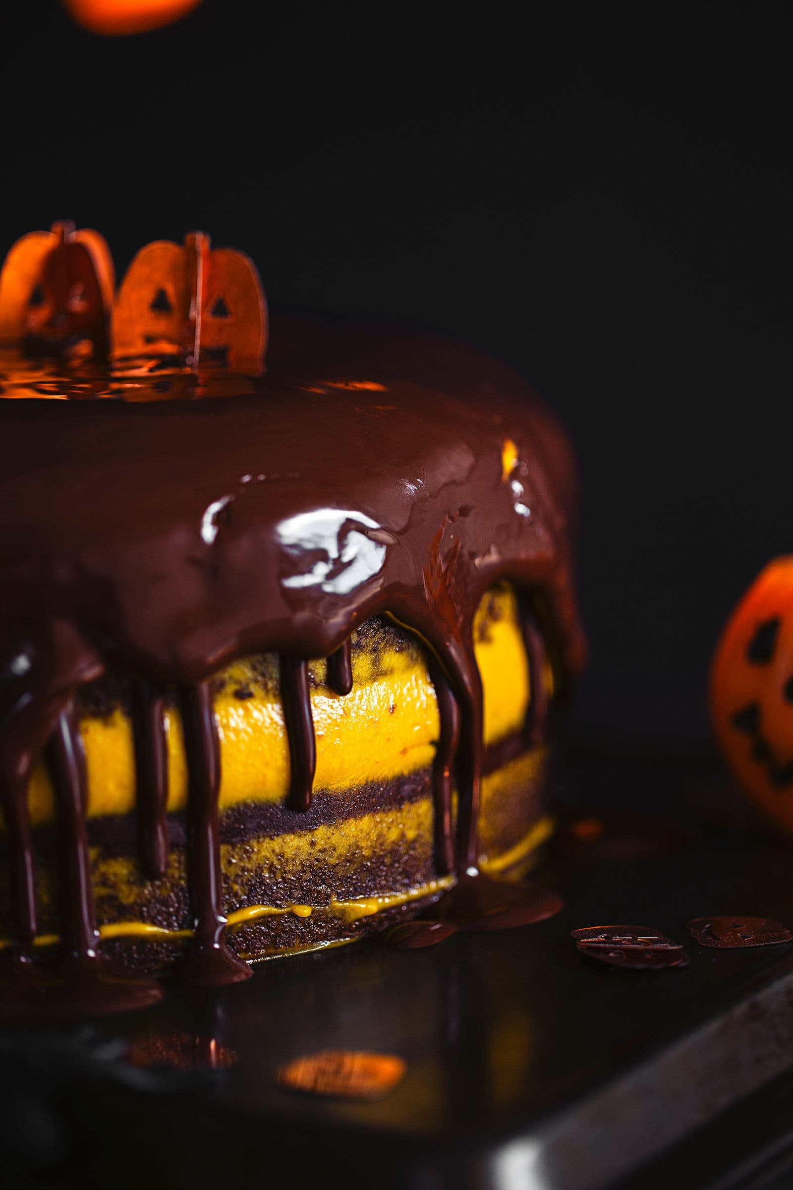 Detail shot of chocolate glaze dripping over a layered cake with bright orange filling for Halloween.